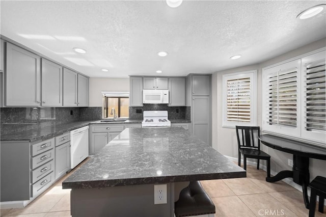 kitchen with a kitchen island, gray cabinetry, dark stone counters, light tile patterned floors, and white appliances