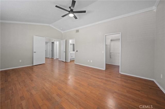 unfurnished bedroom with ensuite bathroom, wood-type flooring, a spacious closet, vaulted ceiling, and ornamental molding