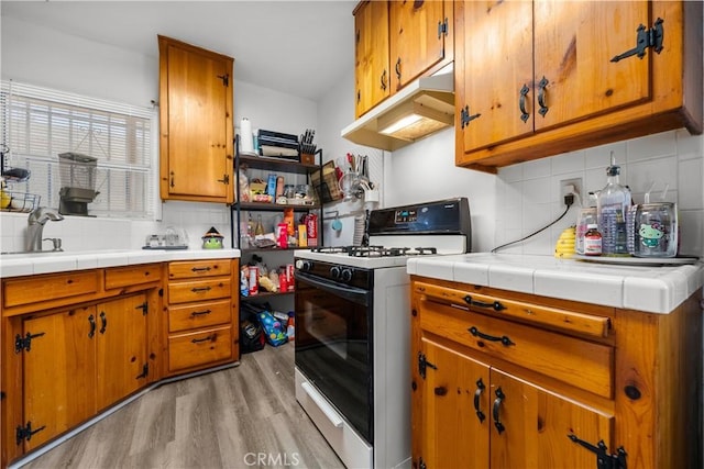 kitchen with sink, light hardwood / wood-style floors, tile countertops, decorative backsplash, and range with gas cooktop