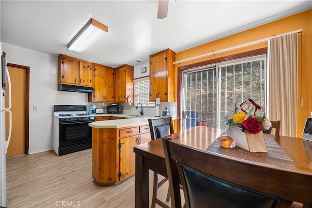 kitchen with sink, gas stove, light hardwood / wood-style flooring, kitchen peninsula, and ceiling fan