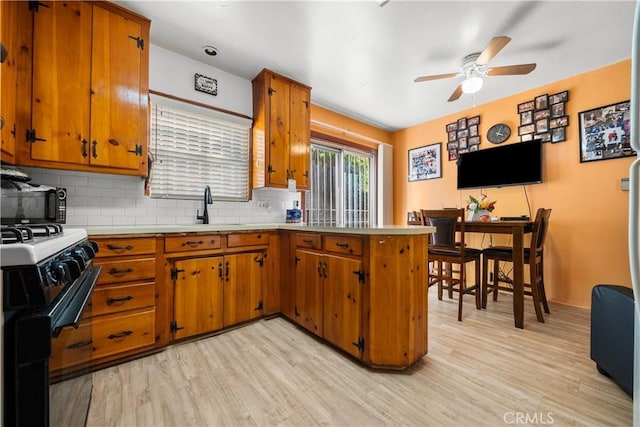 kitchen with gas stove, sink, light hardwood / wood-style floors, and decorative backsplash