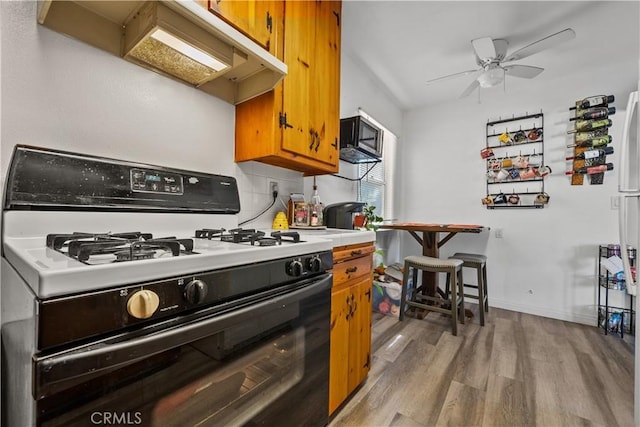 kitchen with premium range hood, ceiling fan, black gas range, and light hardwood / wood-style flooring