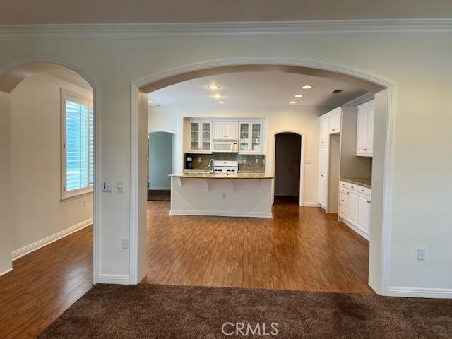 kitchen with a breakfast bar area, white cabinetry, crown molding, dark hardwood / wood-style floors, and backsplash