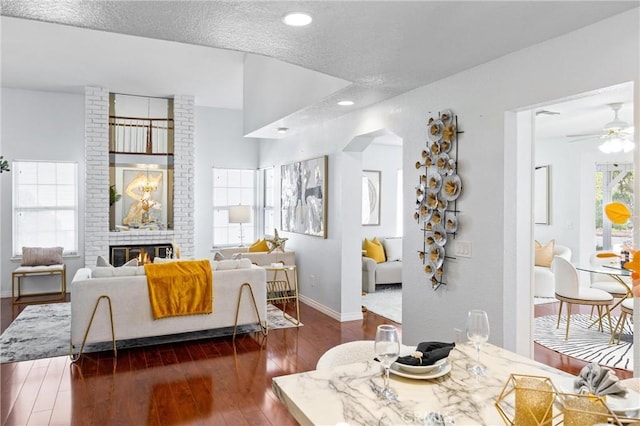 interior space featuring a brick fireplace, dark hardwood / wood-style floors, a textured ceiling, and ceiling fan