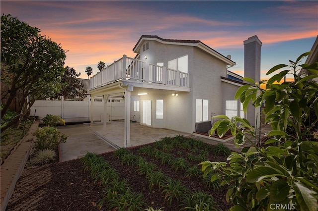 back house at dusk featuring a balcony and a patio