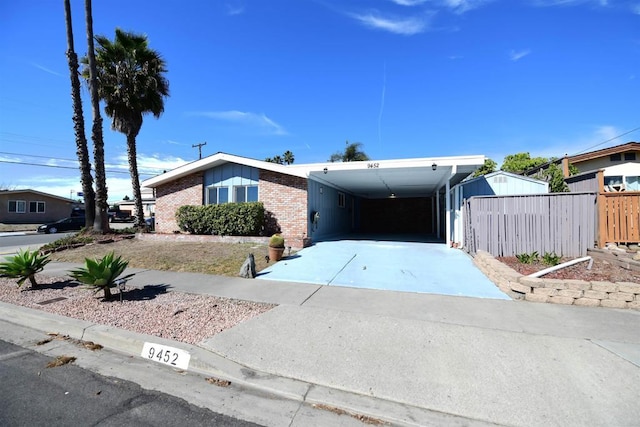 mid-century modern home with driveway, an attached carport, fence, and brick siding