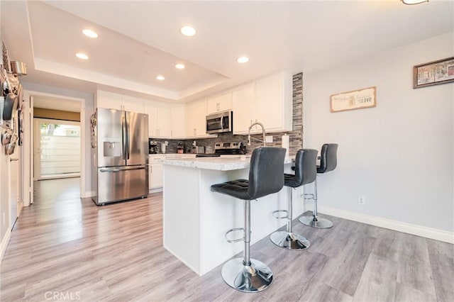 kitchen with a breakfast bar, white cabinetry, appliances with stainless steel finishes, a tray ceiling, and decorative backsplash