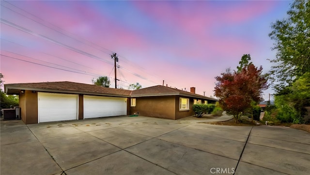 ranch-style home featuring a garage, driveway, a chimney, and stucco siding