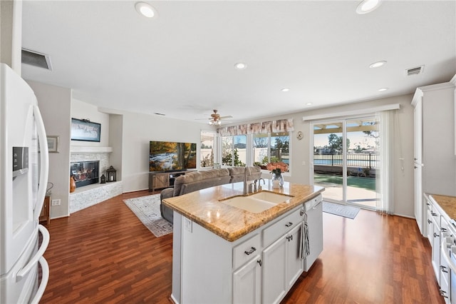 kitchen featuring white cabinetry, sink, a kitchen island with sink, light stone counters, and white appliances