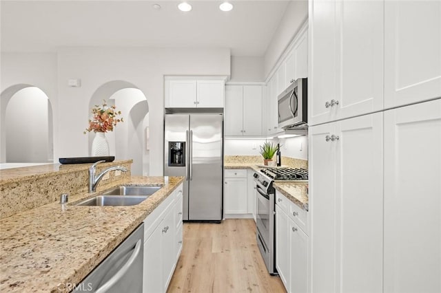 kitchen with white cabinetry, sink, stainless steel appliances, light stone countertops, and light hardwood / wood-style flooring