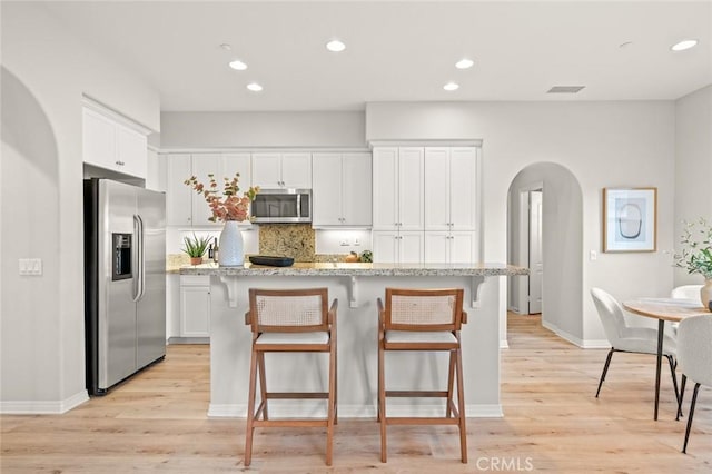 kitchen featuring appliances with stainless steel finishes, white cabinetry, light stone counters, an island with sink, and light wood-type flooring