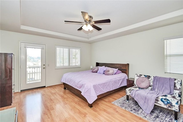 bedroom with a tray ceiling, access to exterior, hardwood / wood-style floors, and ceiling fan