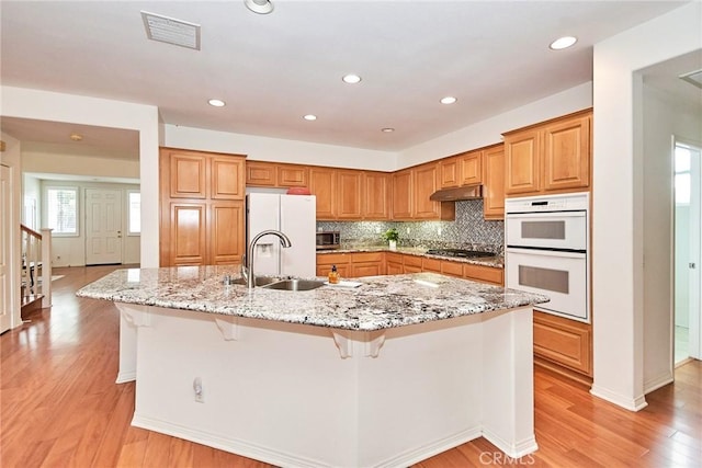 kitchen with a large island, white appliances, light stone countertops, a breakfast bar, and sink