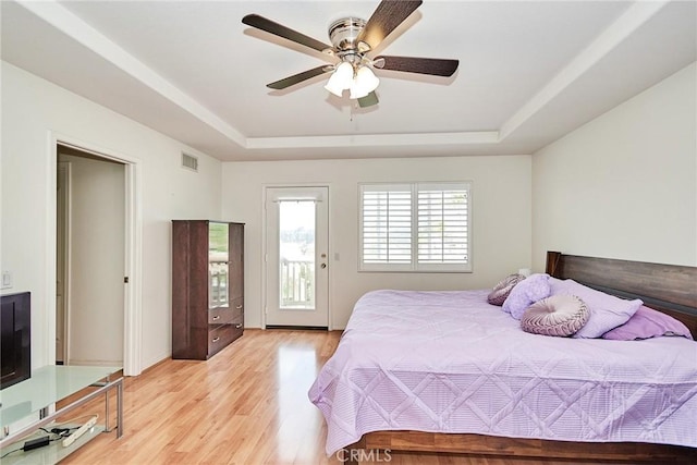 bedroom featuring a tray ceiling, access to exterior, ceiling fan, and light hardwood / wood-style floors