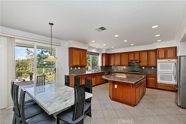 kitchen with sink, gas stovetop, a center island, stainless steel fridge, and pendant lighting