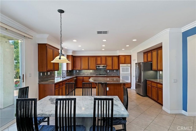 kitchen featuring sink, ventilation hood, stainless steel fridge, a kitchen island, and pendant lighting