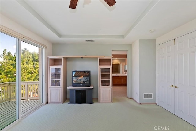 unfurnished living room with light carpet, ceiling fan, and a tray ceiling