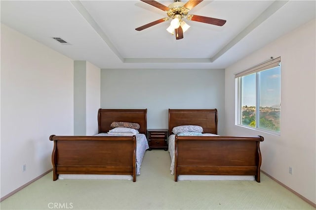 carpeted bedroom with a raised ceiling and ceiling fan