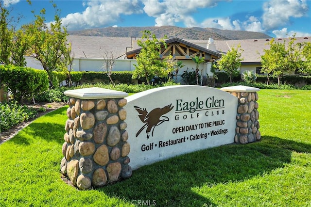 community sign with a mountain view and a yard