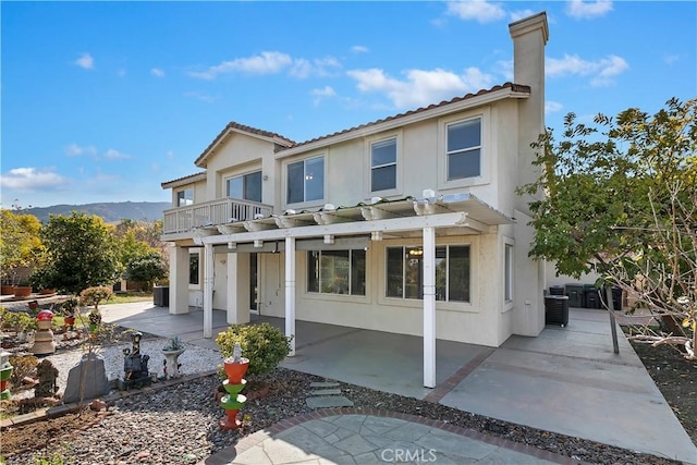 rear view of house featuring a balcony, central air condition unit, a pergola, a mountain view, and a patio area