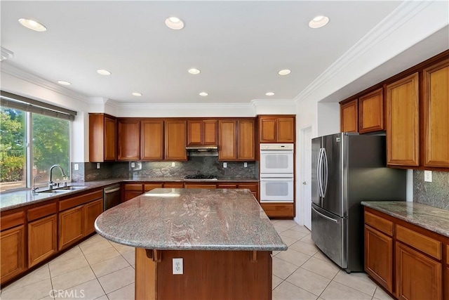 kitchen featuring sink, stainless steel refrigerator, double oven, a center island, and light stone countertops