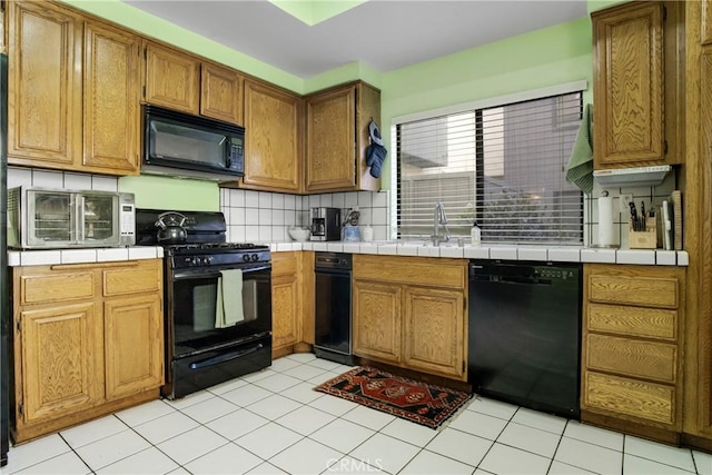 kitchen with tasteful backsplash, tile countertops, brown cabinets, black appliances, and a sink