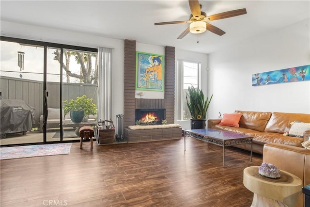 living area with ceiling fan, a brick fireplace, and wood finished floors