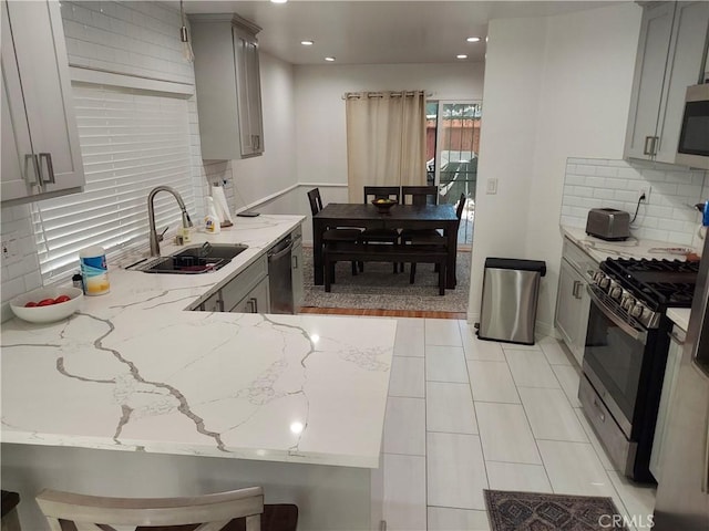 kitchen with light stone counters, tasteful backsplash, gray cabinets, appliances with stainless steel finishes, and a sink