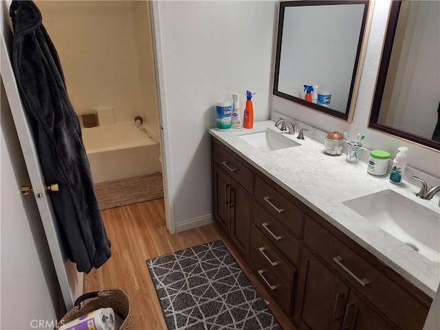 bathroom featuring double vanity, wood finished floors, a sink, and baseboards