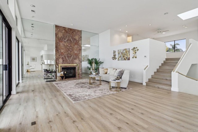 living room featuring a skylight, a towering ceiling, a high end fireplace, and light wood-type flooring