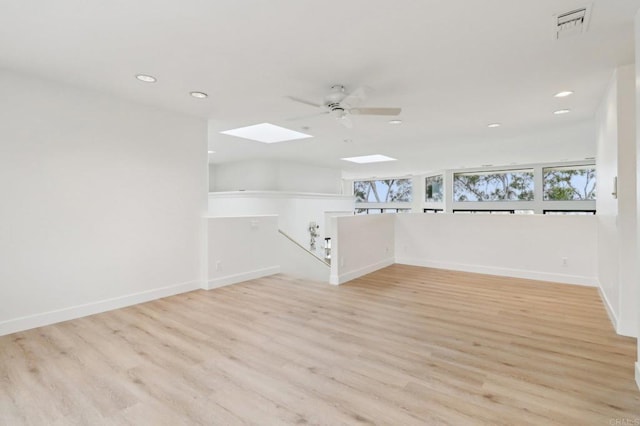 unfurnished room featuring a skylight, ceiling fan, and light hardwood / wood-style flooring