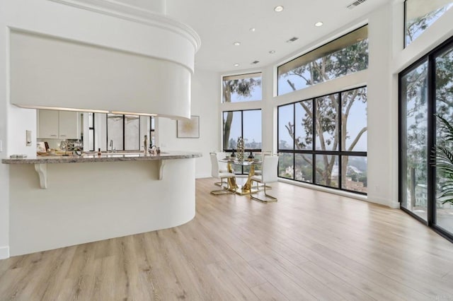 interior space featuring a kitchen bar, light stone counters, light hardwood / wood-style flooring, kitchen peninsula, and a high ceiling