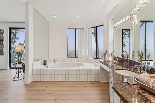 bathroom featuring vanity, a healthy amount of sunlight, hardwood / wood-style floors, and tiled bath