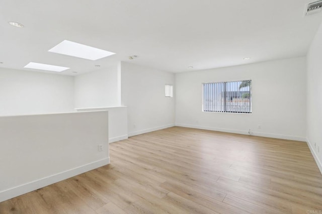 empty room featuring a skylight and light wood-type flooring