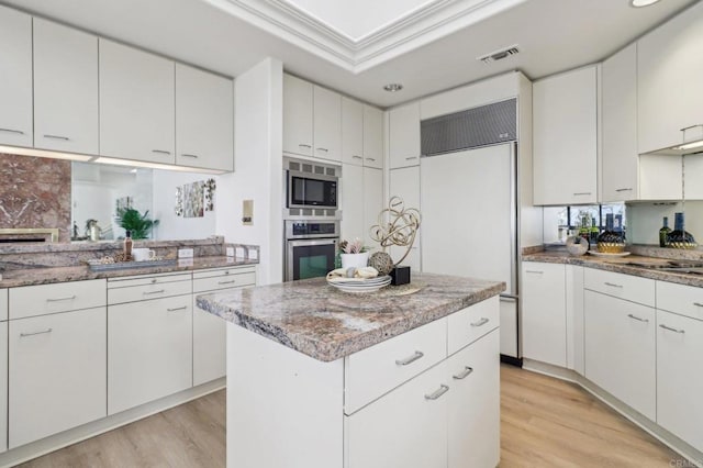 kitchen with built in appliances, white cabinetry, light hardwood / wood-style flooring, and a center island