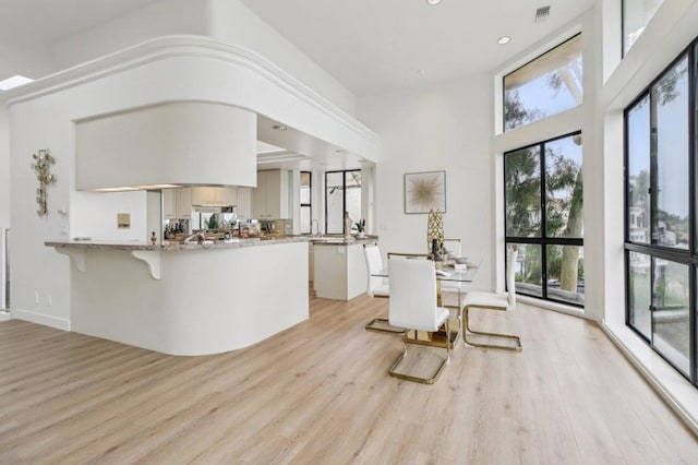 kitchen with white cabinets, a high ceiling, kitchen peninsula, light stone countertops, and light wood-type flooring