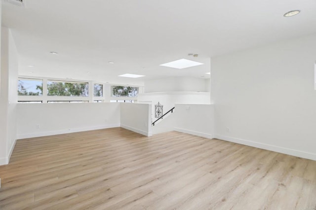 empty room with a skylight and light hardwood / wood-style flooring