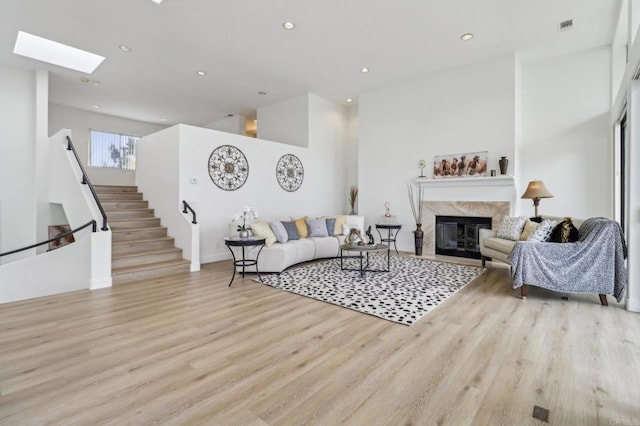 living room featuring a skylight, a fireplace, light hardwood / wood-style floors, and a high ceiling