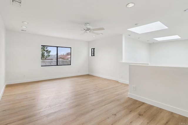 spare room with ceiling fan, light wood-type flooring, and a skylight