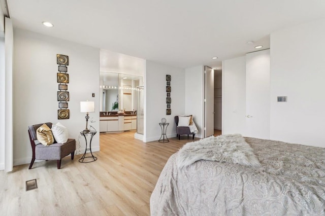 bedroom with a walk in closet, ensuite bath, and light hardwood / wood-style flooring