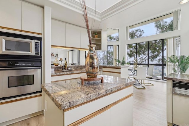 kitchen with light hardwood / wood-style flooring, appliances with stainless steel finishes, white cabinetry, light stone countertops, and ornamental molding