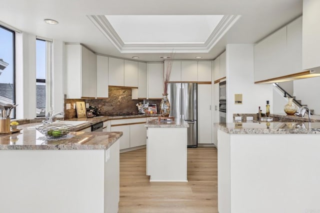 kitchen with appliances with stainless steel finishes, a tray ceiling, white cabinets, and kitchen peninsula