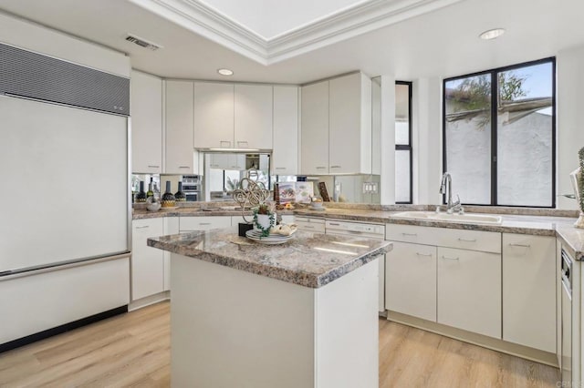 kitchen featuring sink, built in fridge, a center island, white cabinets, and a raised ceiling