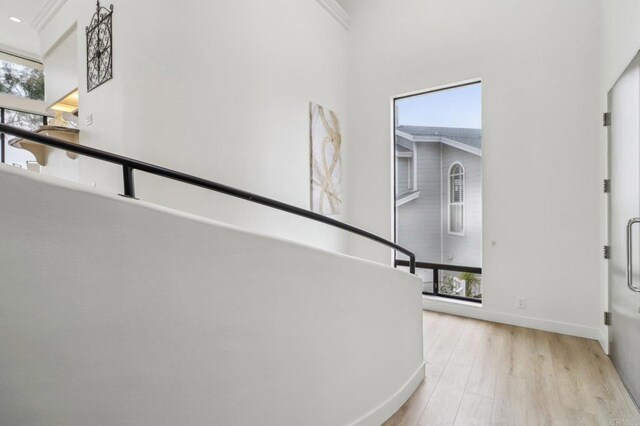 hall with ornamental molding, a towering ceiling, and light hardwood / wood-style floors