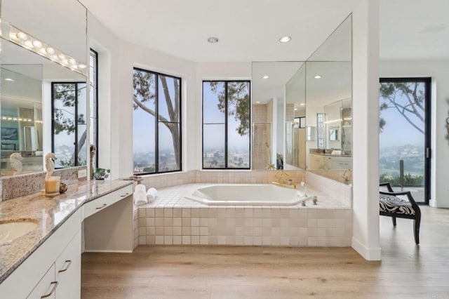 bathroom featuring wood-type flooring, tiled bath, and vanity