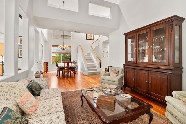 living area with a towering ceiling, an inviting chandelier, wood finished floors, baseboards, and stairs