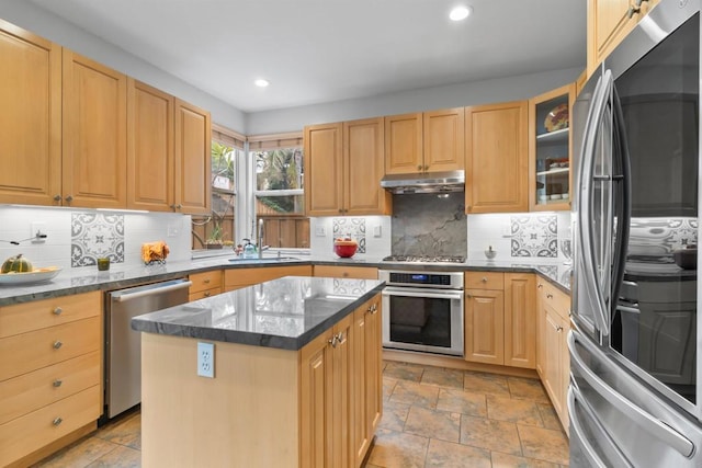 kitchen with glass insert cabinets, appliances with stainless steel finishes, a center island, under cabinet range hood, and a sink