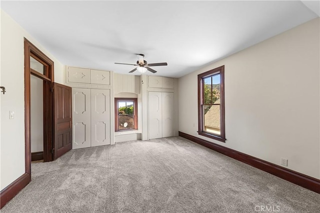 unfurnished bedroom featuring ceiling fan, carpet flooring, and two closets