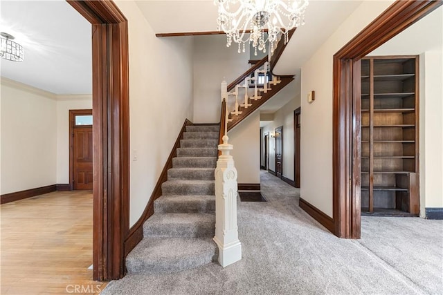 stairway featuring ornamental molding, carpet floors, an inviting chandelier, and built in shelves