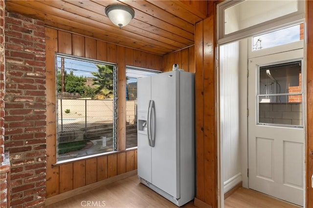 kitchen with light wood-type flooring, wood ceiling, white refrigerator with ice dispenser, and wood walls